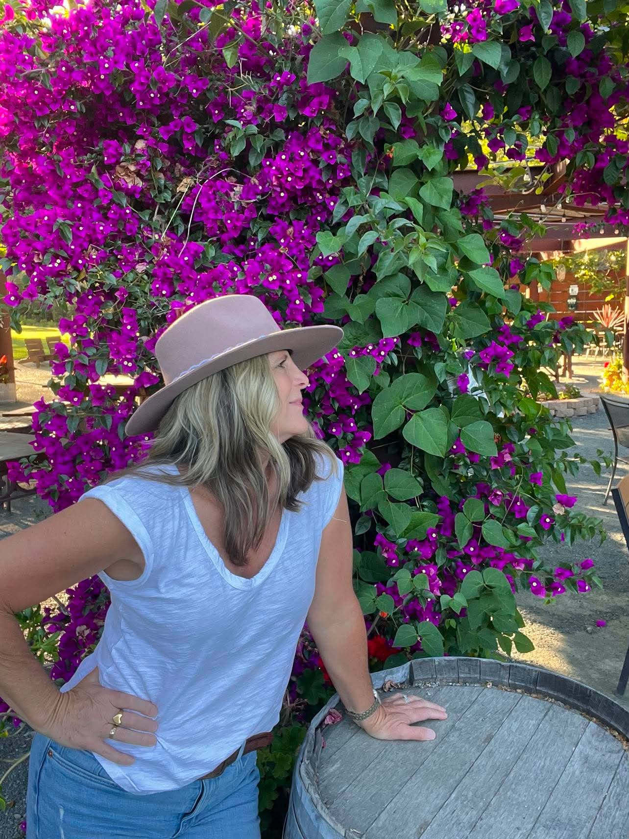 Phyllis in a wide-brimmed hat beside a flowering bougainvillea arbor